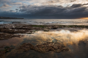 Seascape sunrise long exposure with calm water puddle and grim sky