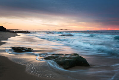 Soft sunrise colors reflect on the water at Blackwoods Beach, offering a peaceful scene for coastal photography.