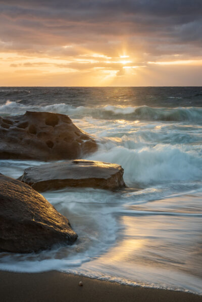 Warm morning light bathes the waves and rocks at Blackwoods Beach, showcasing the beauty of the sunrise.