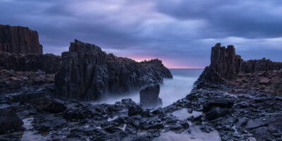 Dusk light casting shadows over the imposing rock formations at Bombo headland, embodying ocean artwork.