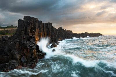 Powerful waves creating a Primal Pulse against Bombo Quarry's rock formations, epitomizing ocean art.