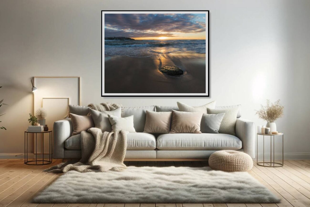 In the living room, a framed art piece captures the first light of sunrise bathing Bondi Beach in a golden glow, creating an enchanting ocean artwork display. This piece adds warmth and a serene ambiance to the space, inviting viewers to bask in the beauty of the dawn's gentle illumination.