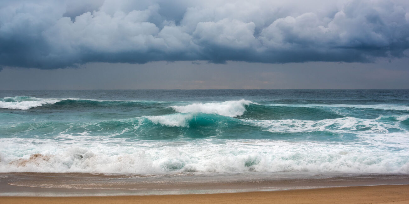 Peaceful waves roll onto the sandy shore of Bronte Beach beneath a dramatic sky, hinting at the storm to come.