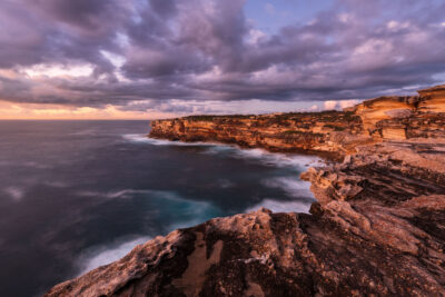 Early morning light bathes the cliffs of Cape Solander in soft lavender and orange.