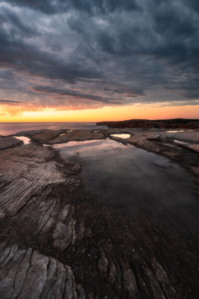 Cape Solander at sunrise with dark clouds and a hint of light reflecting on water.