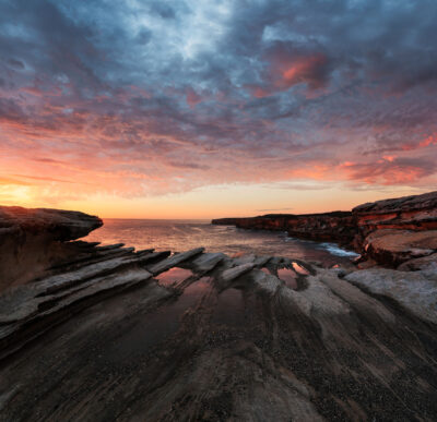 Dramatic sunrise with a fiery sky above the rugged coastline of Cape Solander in a square print.