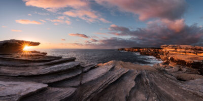 Sunrise panorama at Cape Solander revealing a golden sunburst among the rocks.