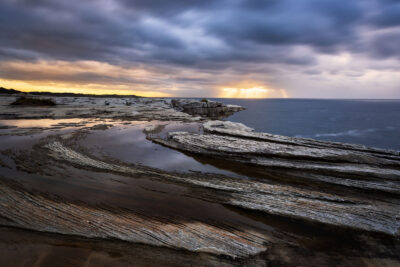 Sunrise illuminating the swirling rock formations along the Cape Solander coastline.