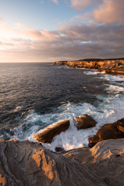 Sunrise casting a golden blaze on the cliffs and turbulent sea at Cape Solander