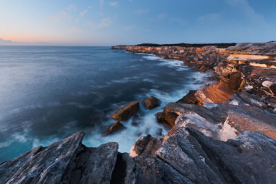 Early morning tranquility at Cape Solander with gentle blue waves and amber sunrise.
