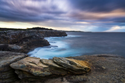 Serene sunrise at Cape Solander with expansive blue sky and sea meeting the rugged coast.