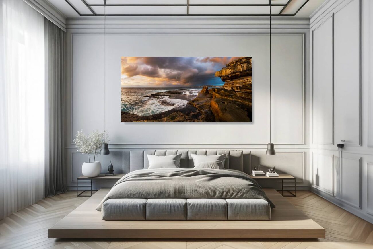 The bedroom's canvas art features the scene at Clovelly Beach where the sun's golden rays highlight the turbulent waves and rugged shores, beneath a stormy sky. This artwork brings a sense of awe and tranquility to the room, ideal for creating a peaceful yet invigorating environment.