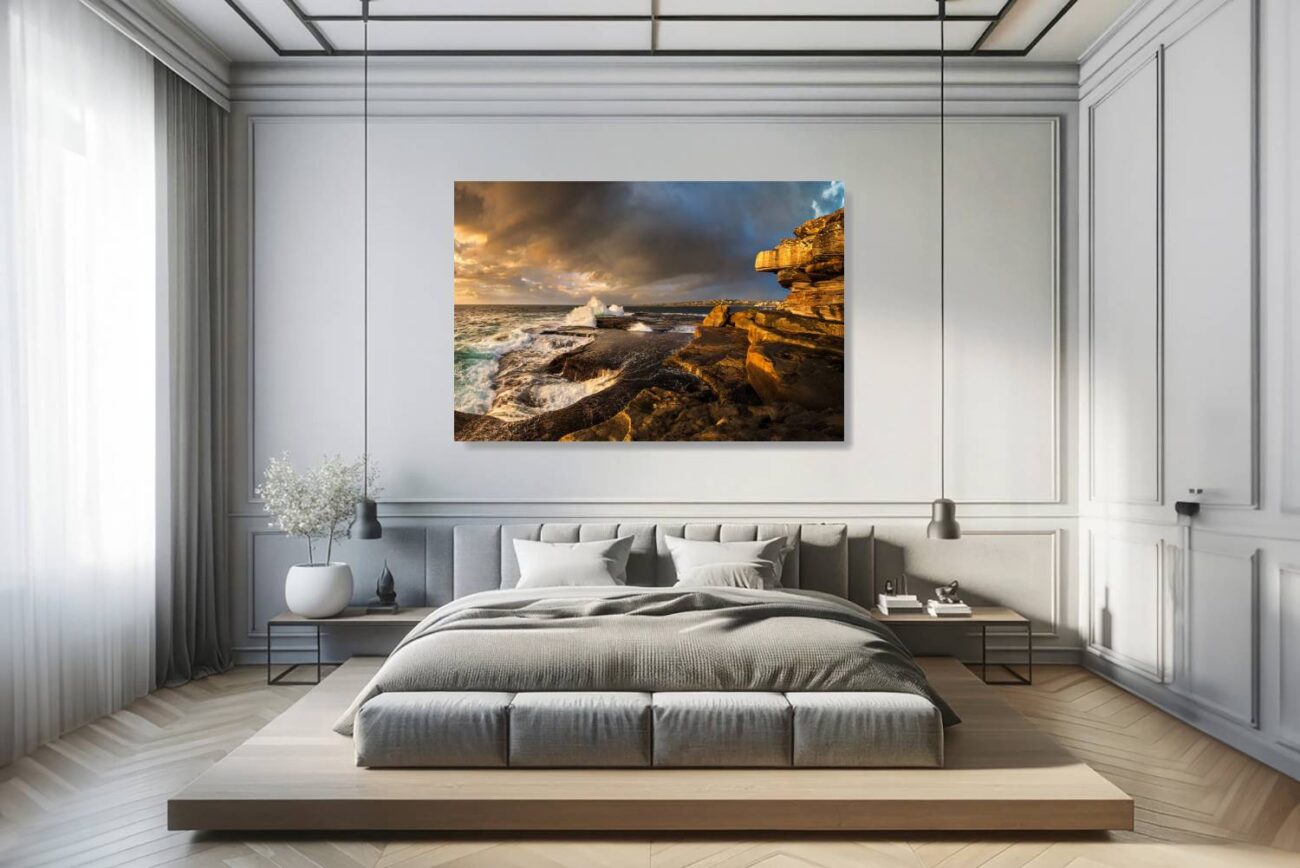 Canvas art in the bedroom features Clovelly Beach at sunrise, where the sunlight illuminates rocks and waves, blending warm and cool hues.