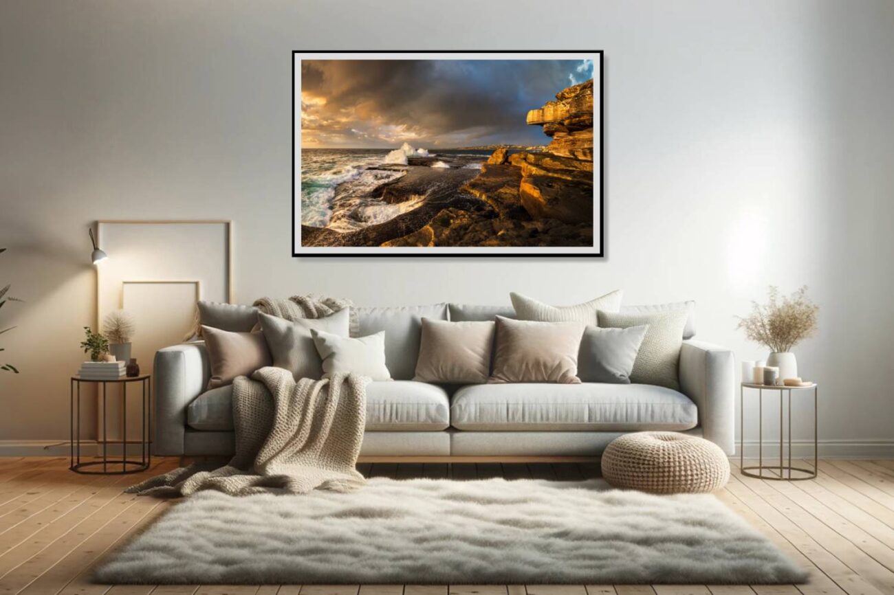 Framed art in the living room showcasing sunrise at Clovelly Beach, highlighting textured rocks and foamy waves against the warm sky and deep blue sea.