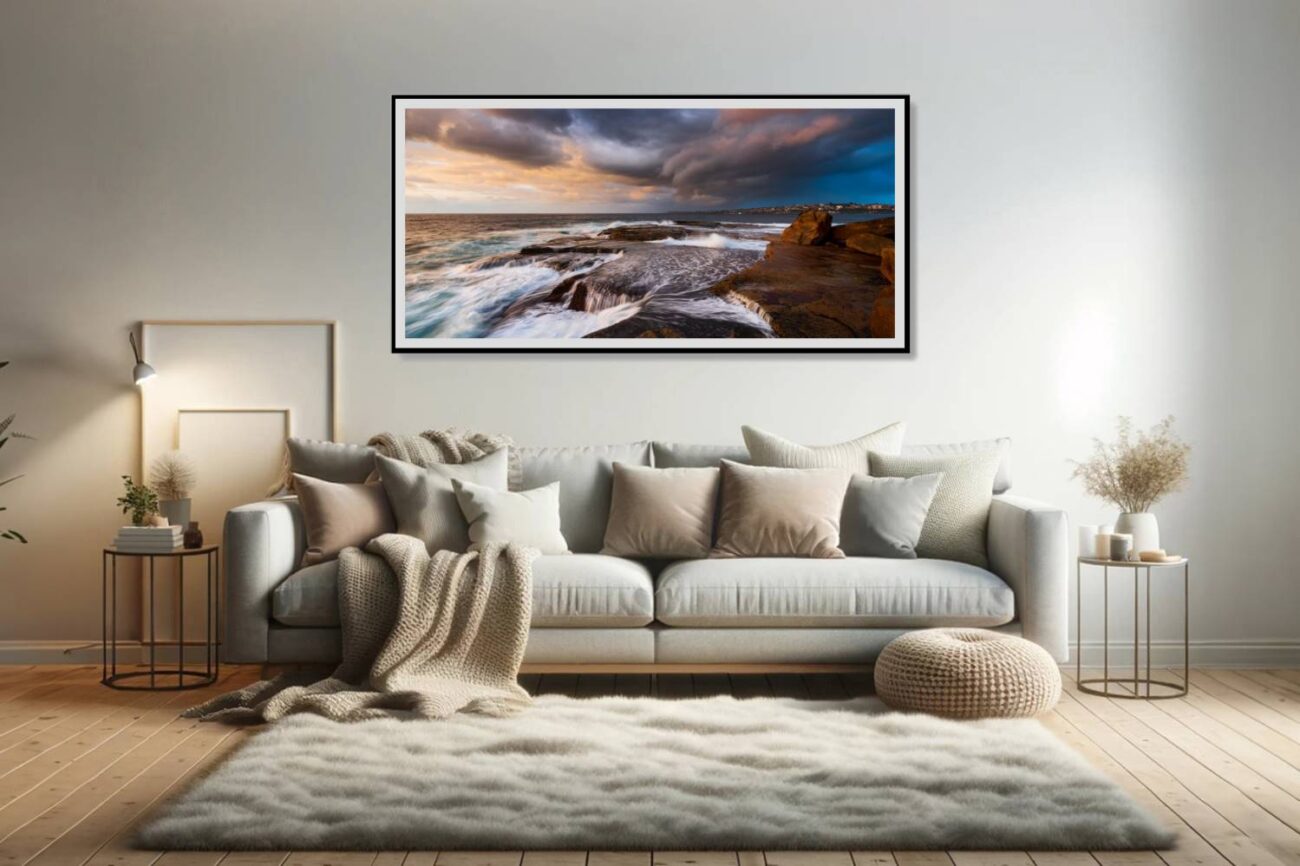 The living room showcases "Indigo Fury," an ocean print capturing the dynamic sunrise at Clovelly Beach under stormy skies, with waves crashing against the shore. This artwork adds a dramatic and powerful element to the space, inviting viewers to feel the intensity and beauty of a tempestuous sea.