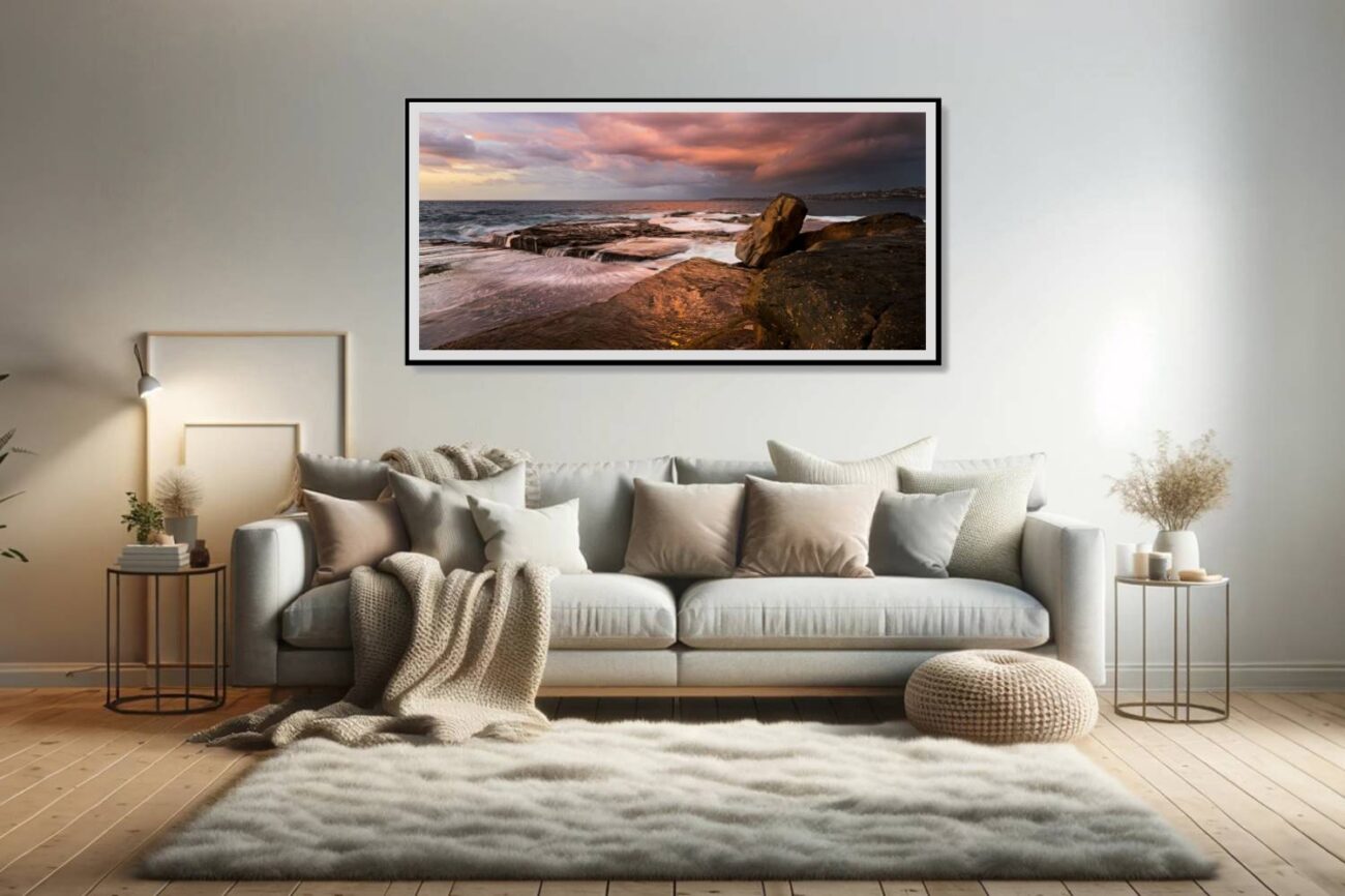 The living room features a framed art piece of a dramatic sunrise at Clovelly Beach, where storm clouds reflect the sun's fiery colors, creating a striking contrast with the tranquil sea. This artwork brings a dynamic and inspiring element to the space, blending the intensity of the sky with the calmness of the ocean.