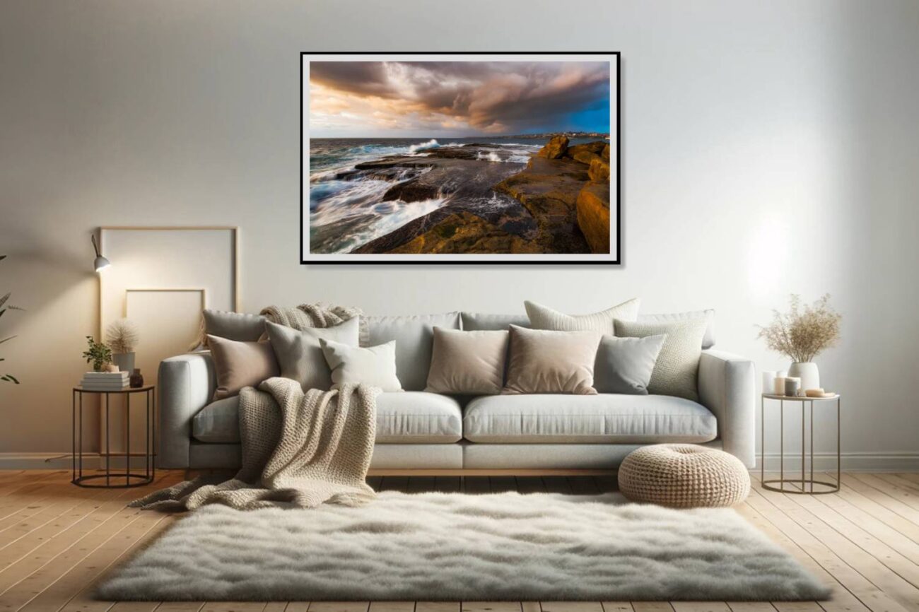 In the living room, a framed art piece captures the first light of day peeking through storm clouds over Clovelly Beach, emphasizing the dramatic interplay between the rugged shoreline and the churning ocean waves. This artwork adds a dynamic and contemplative element to the space, inviting viewers to engage with the powerful forces of nature.