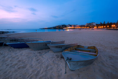 Slumbering boats on the sandy beach of Coogee under a dusky sky, evoking a peaceful evening.
