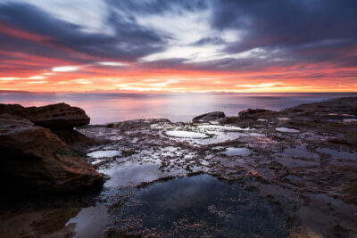 Sunrise at Cronulla beach showcasing a spectrum of orange and purple hues reflecting in tide pools.