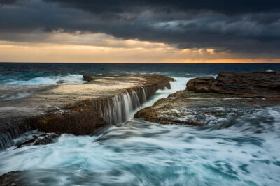 Sunrise at Clovelly Beach with waves crashing like waterfalls, suited for storm artwork or elegant wall pieces.