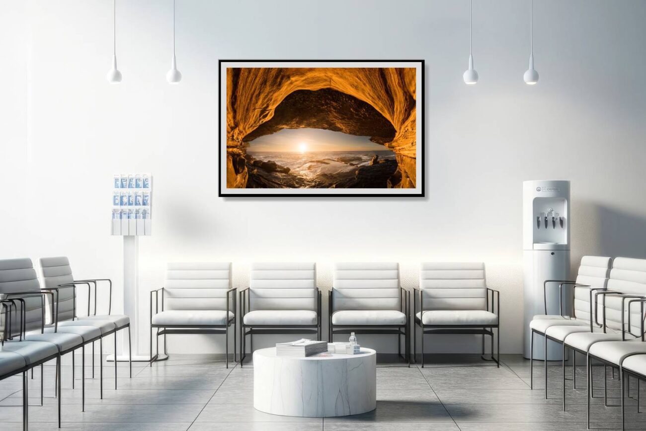 Framed orange wall art in the medical office portrays the sea cave at Clovelly Beach, where the sunrise creates an eye-like effect with the cave entrance. This intriguing and warm artwork adds a touch of natural elegance and mystery, enhancing the healing environment with its beautiful and calming presence.