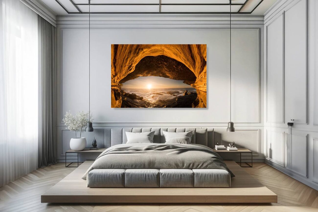 The bedroom's canvas art depicts the sea cave at Clovelly Beach as it frames the sunrise, creating an eye-like illusion with the cave entrance and the sun. This artwork in orange tones brings a serene yet intriguing ambiance to the room, ideal for fostering a peaceful and reflective environment.