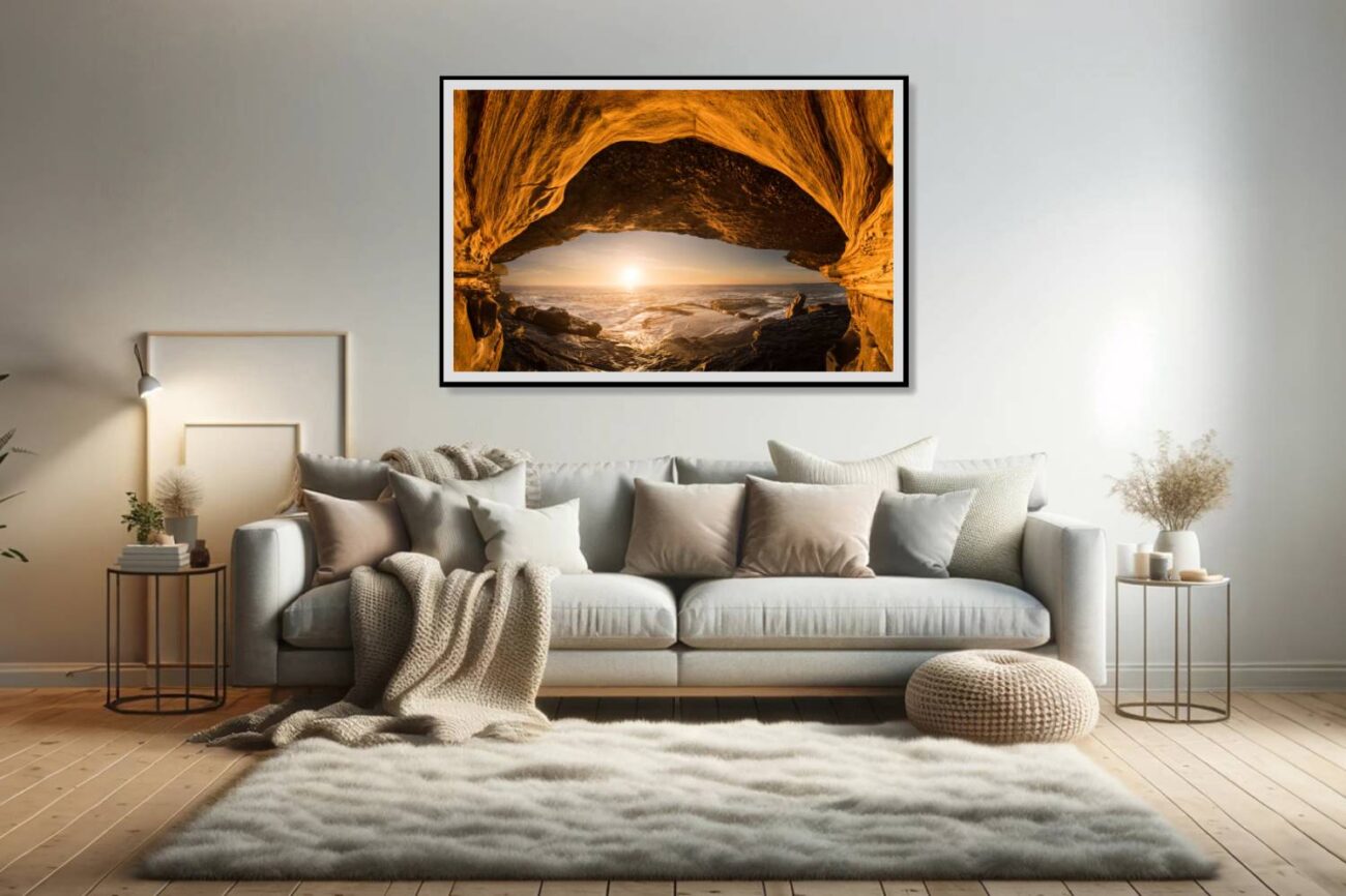 In the living room, a framed orange wall art piece features a sea cave at Clovelly Beach, with the cave entrance and the rising sun creating an eye-like image. This unique perspective adds a mystical and warm touch to the room, inviting viewers to explore the natural beauty and symmetry of the scene.