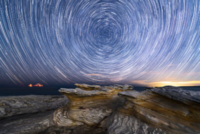 A natural rock formation at Potter Point frames a captivating swirl of star trails in the night sky.