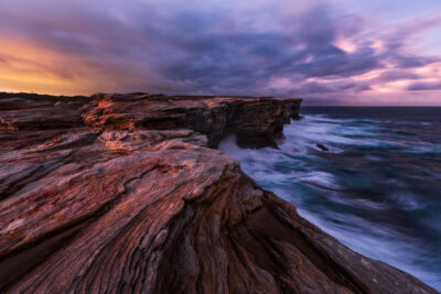 Time-stretched clouds and purple dusk light over ancient sandstone formations at Potter Point.