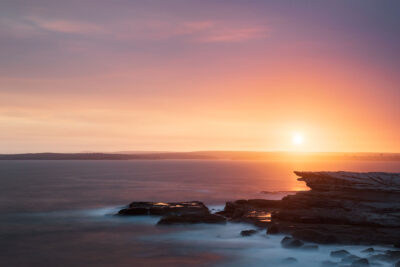 Peaceful seascape at Potter Point under a pastel sky colored by bushfire smoke.