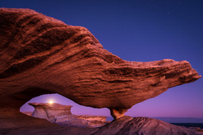 The sandstone formation under a starry sky during moonrise at Potter Point, resembling a dragon.