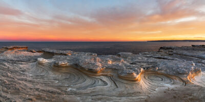 Wind-sculpted sandstone formations at Potter Point bathed in warm sunset light, panoramic shot.