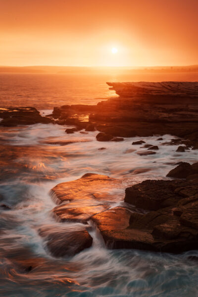 Sunset casting a fiery glow over the waves and rocks at Potter Point.