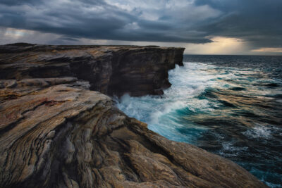 Stormy clouds over the turquoise sea clash with the steadfast sandstone cliffs of Potter Point.