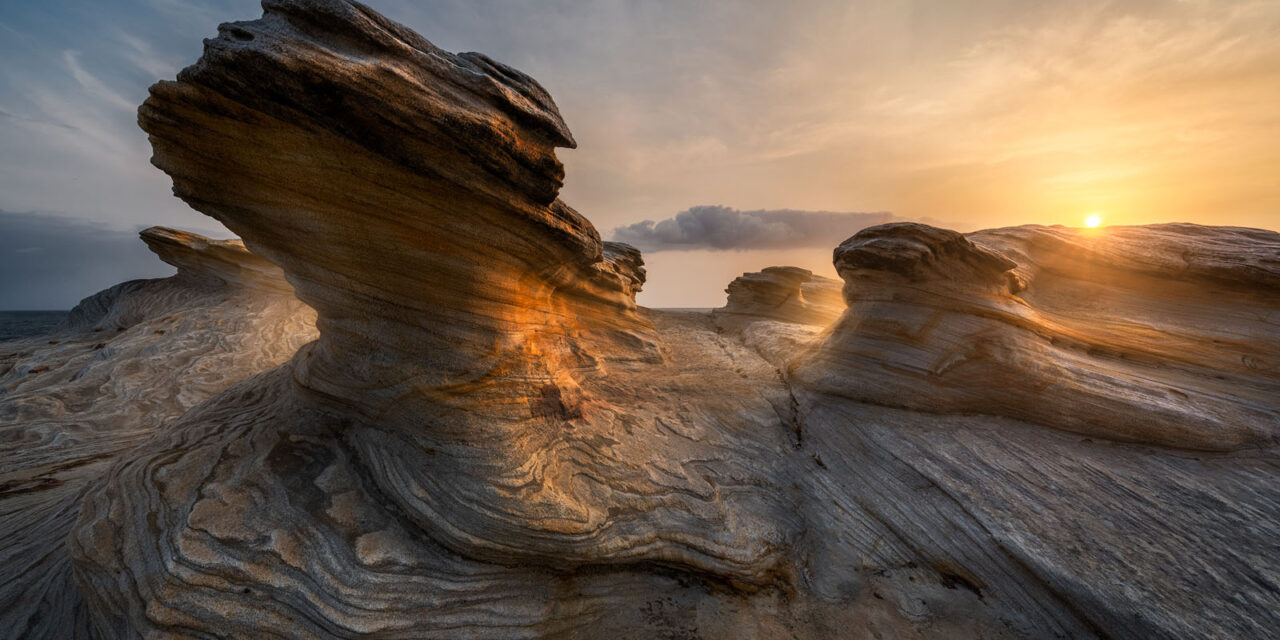 Sunset lights up dragon-like rock formations at Potter Point, with a clear blue sky.