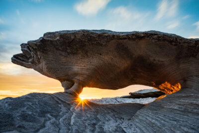 Sunset creating a stunning solar flare through a natural stone archway at Potter Point.