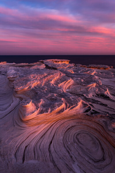 Weathered rock formations at Potter Point under a gradient of lavender and blue sunset hues.
