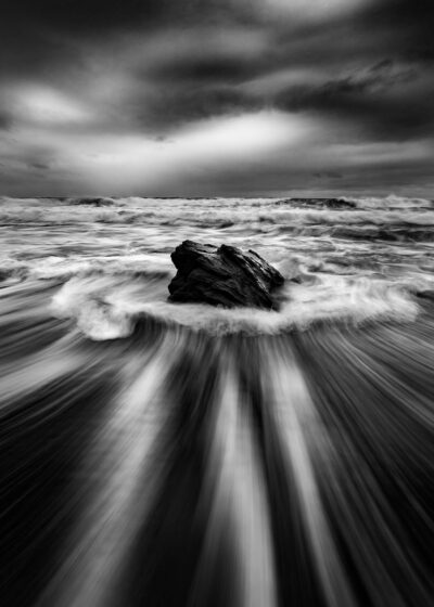 Dramatic black and white wall art of a solitary rock against the powerful ocean currents at Stanwell Beach.