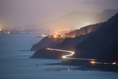 Nighttime view of a winding coastal road with lights at Stanwell Tops, embodying ocean photography.