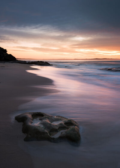 Cronulla beach at sunrise showcasing a rock formation that resembles a Cyclops' face, kissed by the sea.