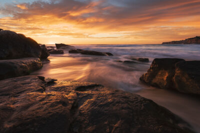 Sunset at Tamarama Beach illuminating the waves and rocks, creating a "Fiery Shores" effect in this ocean artwork.