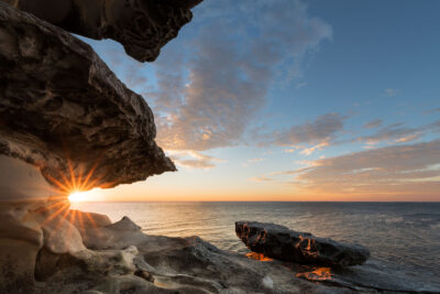 The sun rises through a natural arch at Tamarama Beach, perfect for a beach wall art scene.