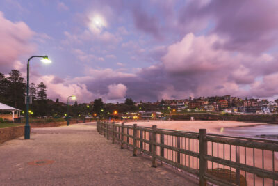 Pathway lit by a streetlamp at Bronte Beach under a twilight sky with purple and pink clouds.