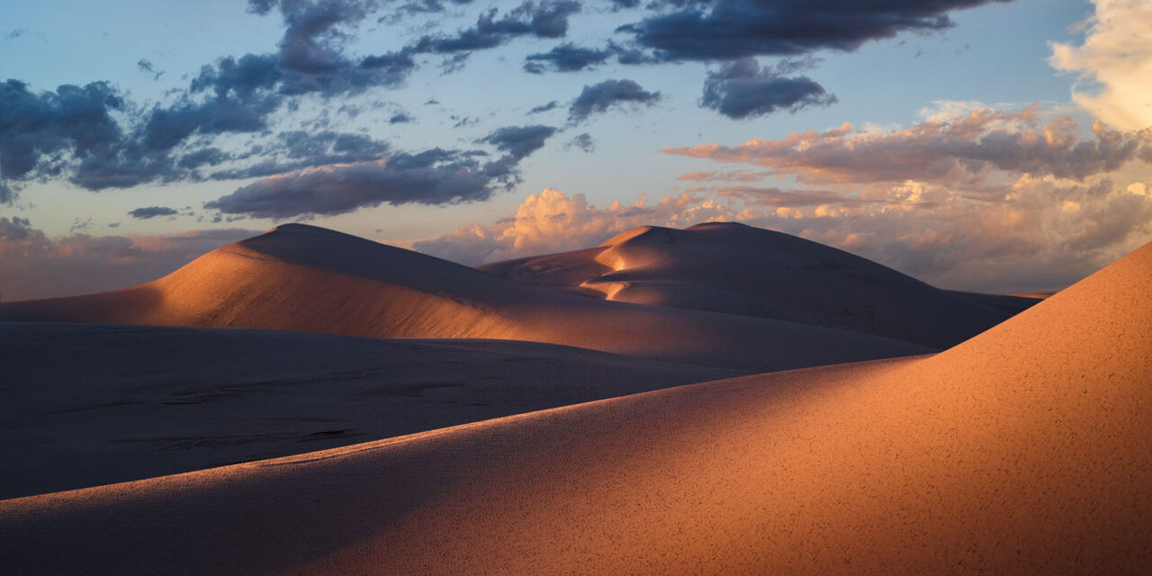 Warm sunlight casting gentle waves of light across sand dunes at dusk.