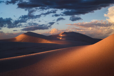 Warm sunlight casting gentle waves of light across sand dunes at dusk.