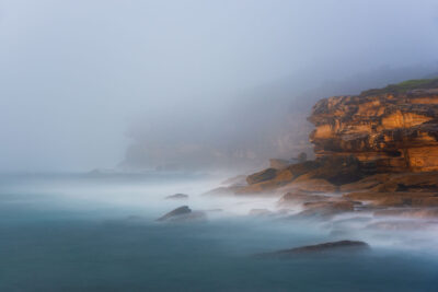 Foggy sunrise at Yena Picnic Point with cliffs shrouded in a tranquil mist over soft waves.