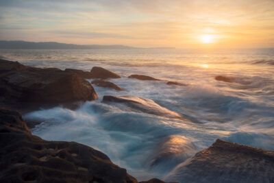 Golden sunrise light illuminates the rolling waves against the rocks at Yena Picnic Point