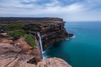A breathtaking waterfall plunges into the sea, framed by the rugged cliffs of Eagle Rock.