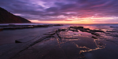 Pink and purple sunrise over calm waters at Bulgo Beach, reflecting symmetry. Violet wall art.
