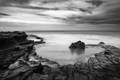 Monochrome art at Garie Beach with a spiraling zen-like pattern of rocks and waves in this tranquil black and white photo.